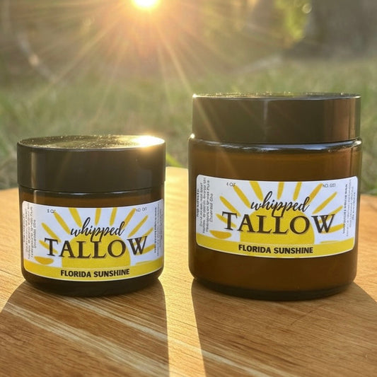 Two jars of 'Whipped Tallow' with a label on a wooden surface with a sunlit background.